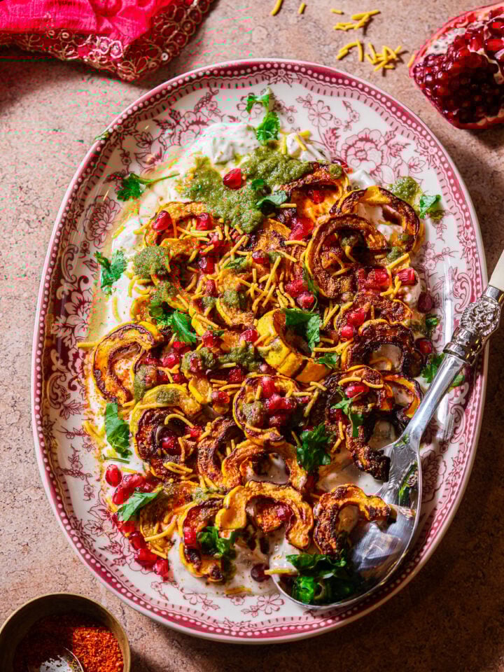 A serving platter filled with roasted delicata squash chaat with a serving spoon.