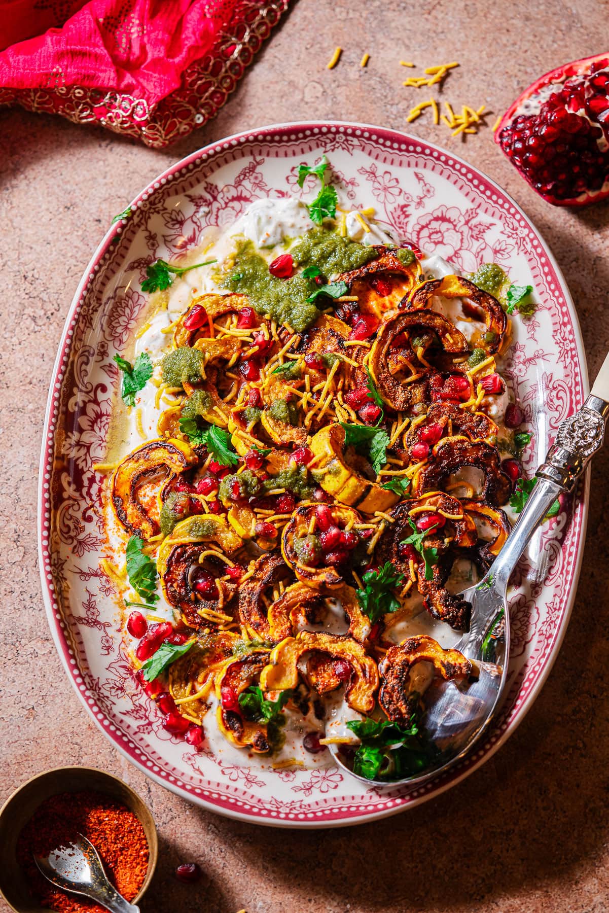 A serving platter filled with roasted delicata squash chaat with a serving spoon.