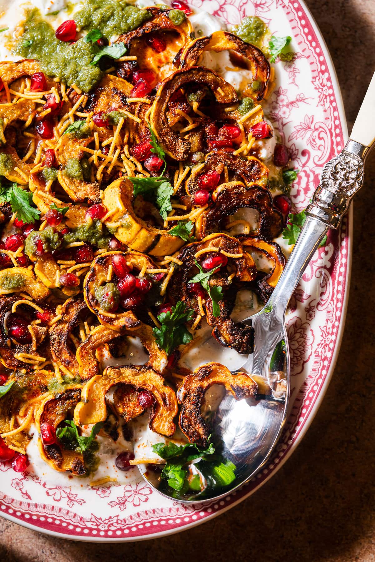A serving platter filled with roasted delicata squash chaat with a serving spoon.