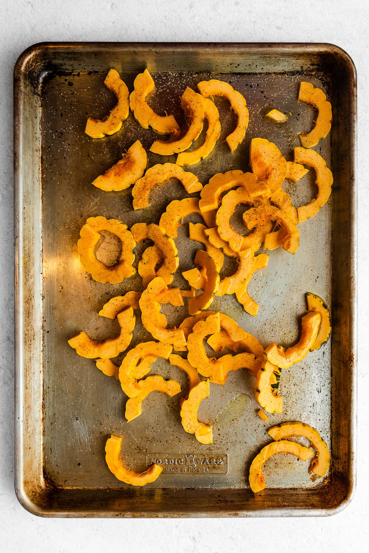 Unroasted seasoned delicata squash in a baking sheet.