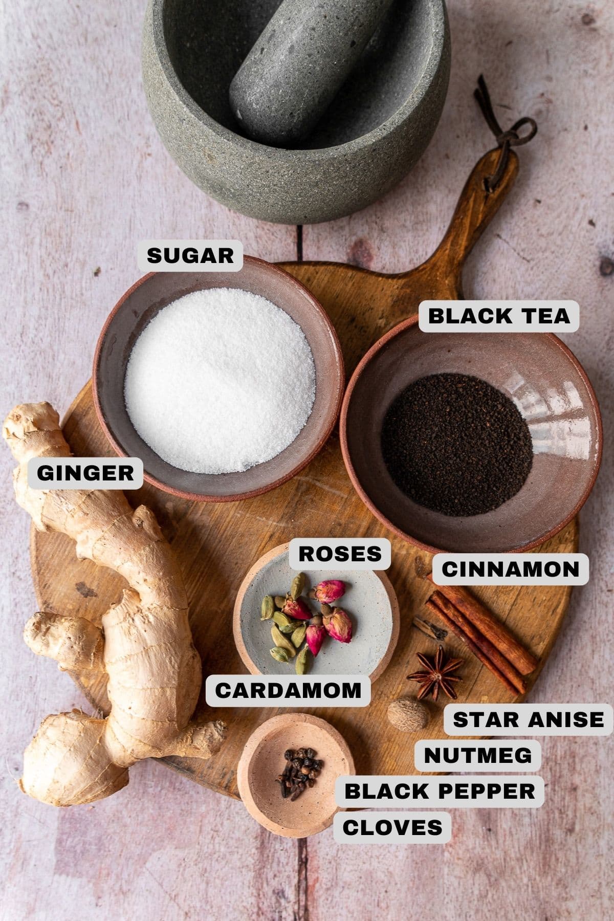 Sugar, black tea, ginger, roses, cardamom, cinnamon, star anise, nutmeg, black pepper, cloves ingredients with labels.