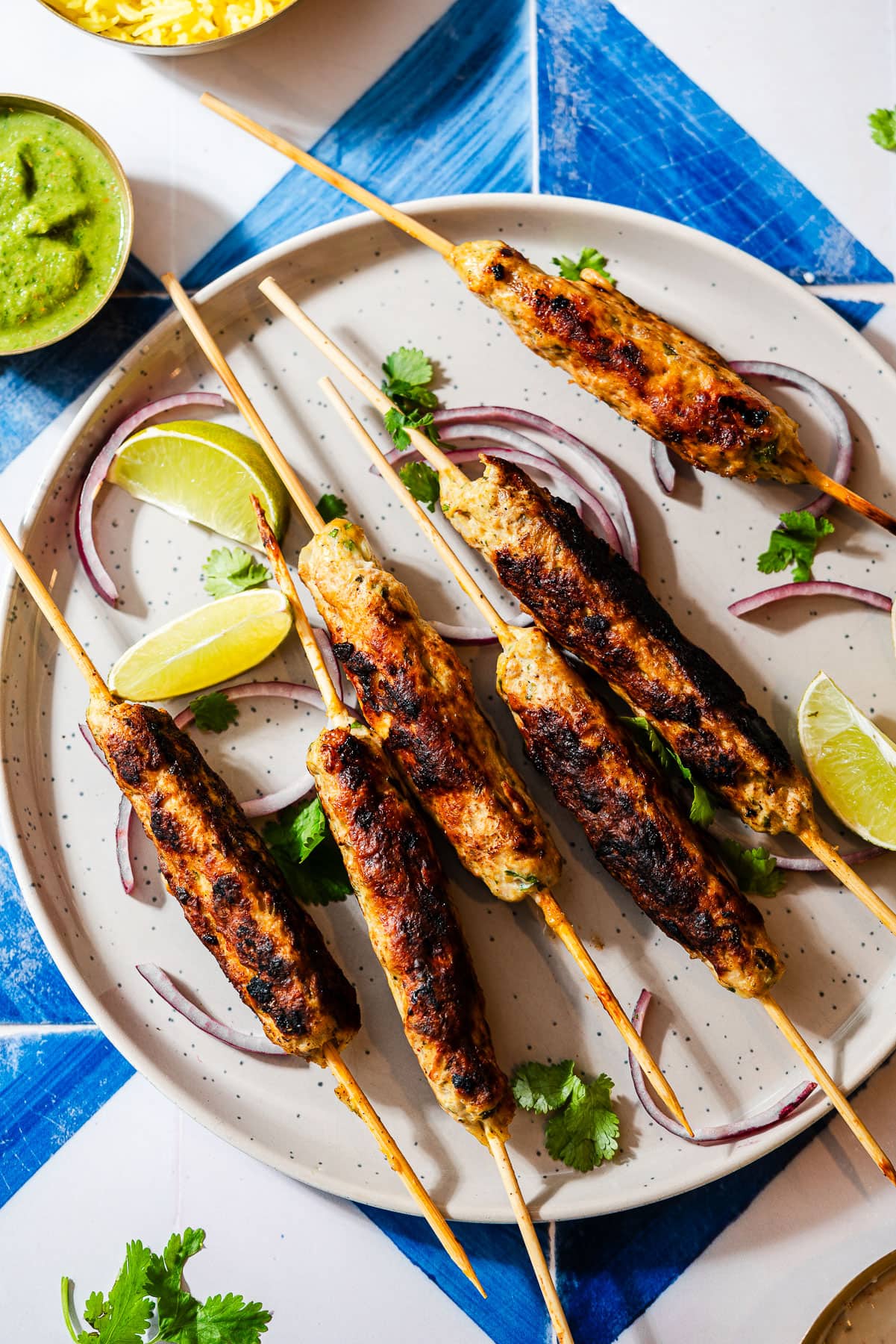 Chicken seekh kebabs on skewers in a plate with limes, onion, and cilantro.