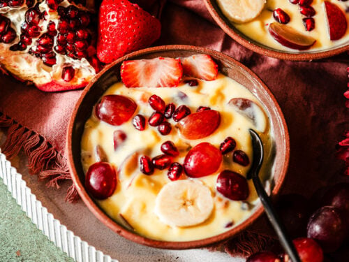 Three dessert bowls of fruit custard in a platter filled with fruits and flowers.