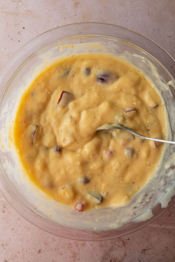 A mixing bowl filled with custard and chopped fruit.
