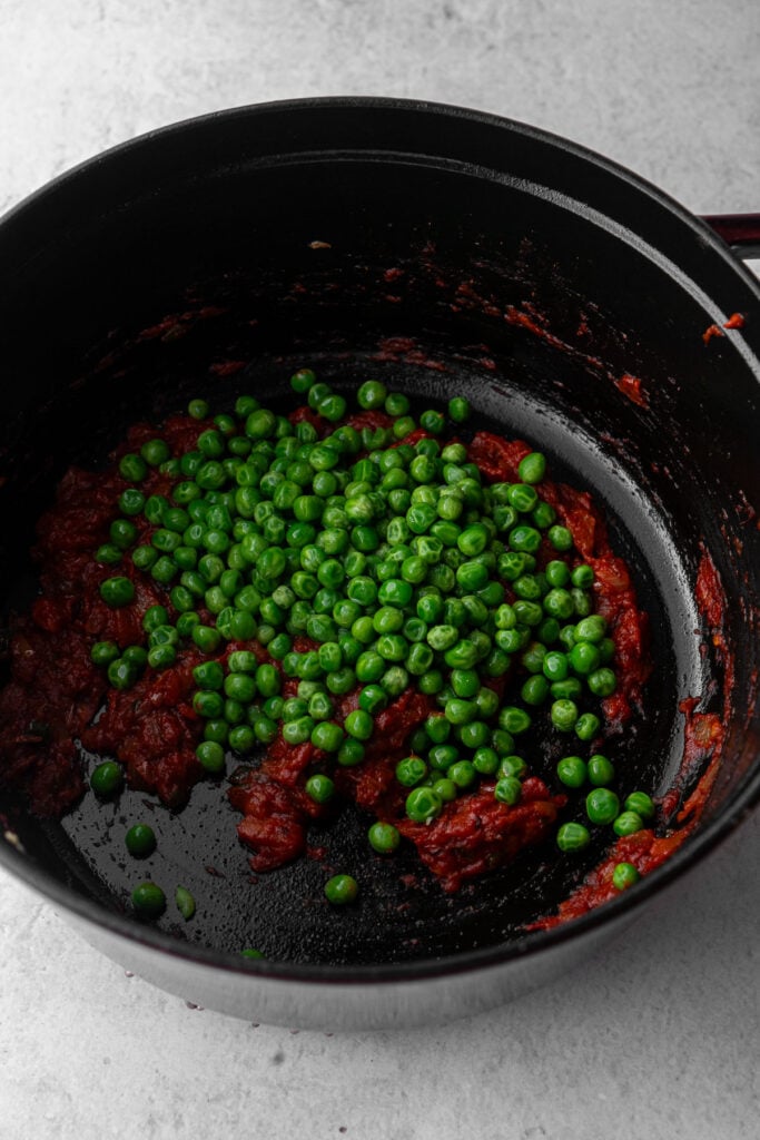 Green peas over cooked down tomato in a dutch oven.
