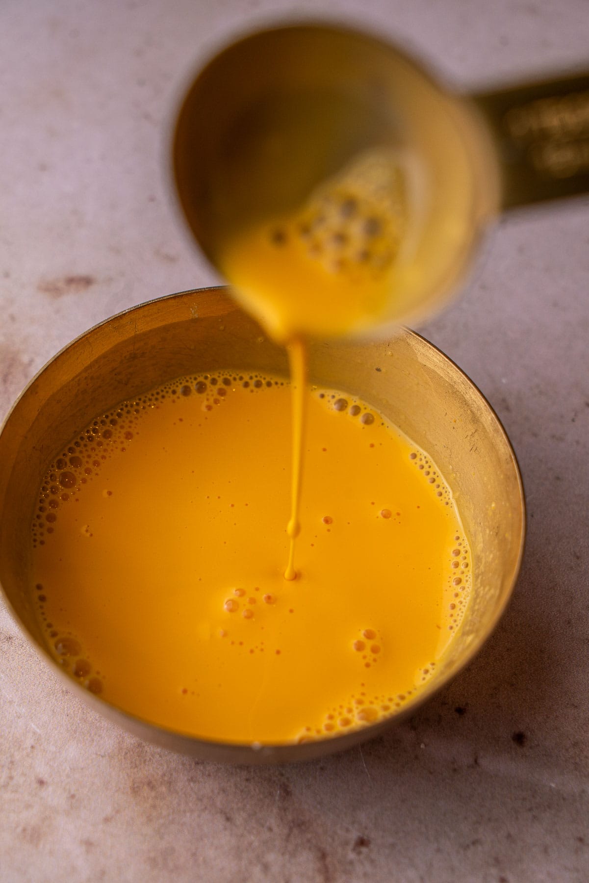 A tablespoon scooping up custard milk from a bowl.