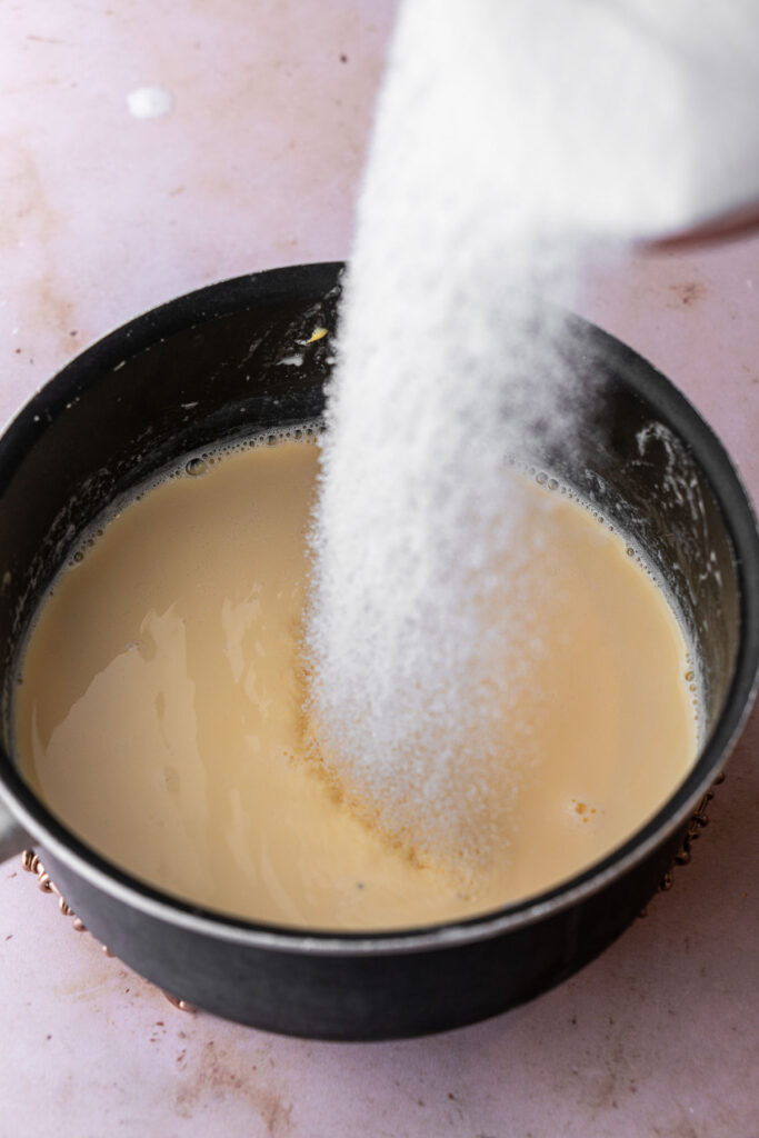 Pouring sugar into a pan of custard milk.