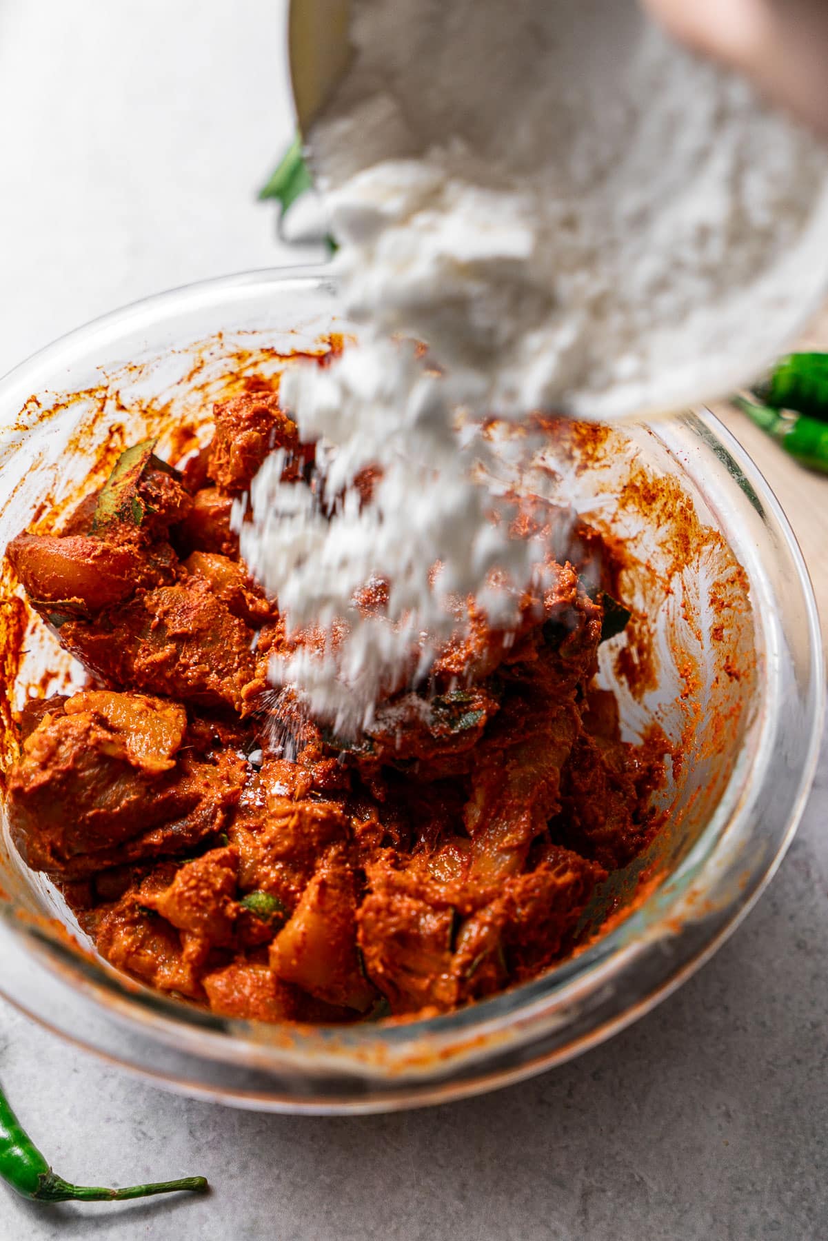 Adding flour to the marinating Chicken 65 in a bowl.