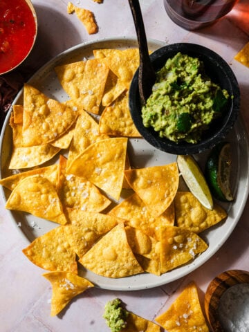 Tortilla chips in a plate with fresh limes, guacamole, and salsa.