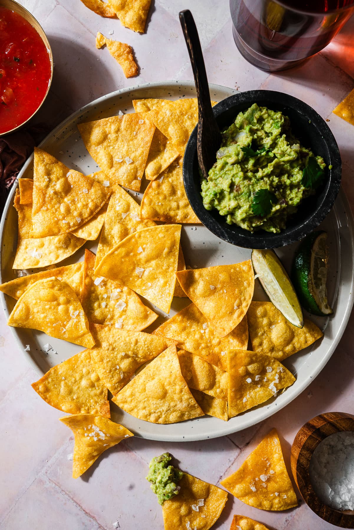 Tortilla chips in a plate with fresh limes, guacamole, and salsa.