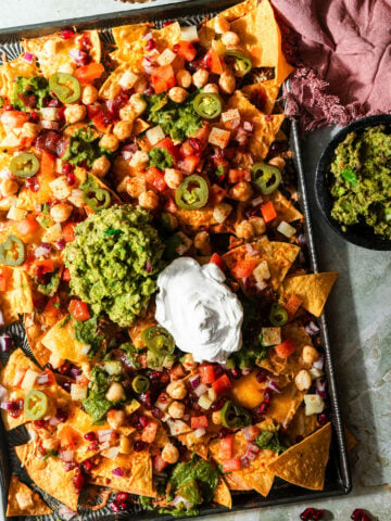 a sheet pan filled with nachos chaat with guacamole and sour cream.
