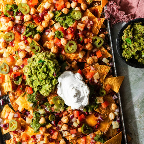 a sheet pan filled with nachos chaat with guacamole and sour cream.