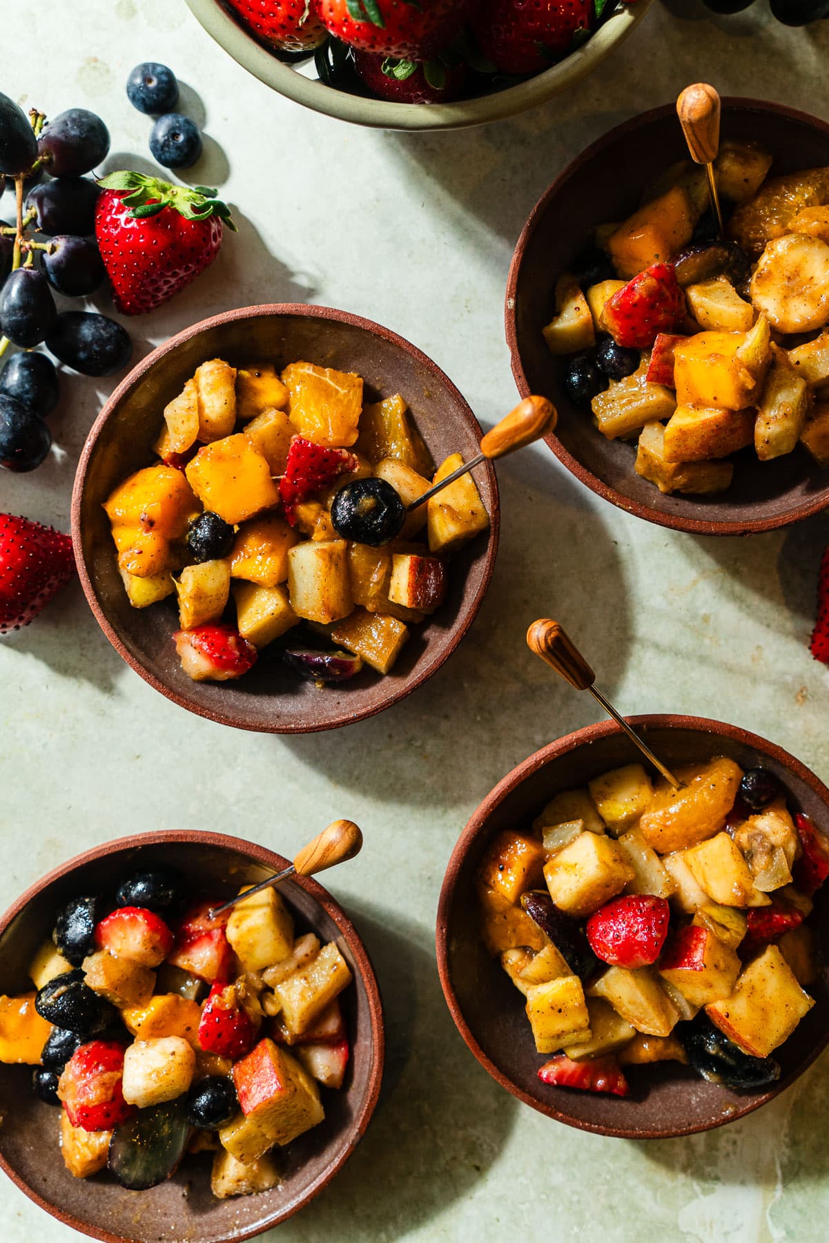 Four bowls filled with fruit chaat with an appetizer pick.