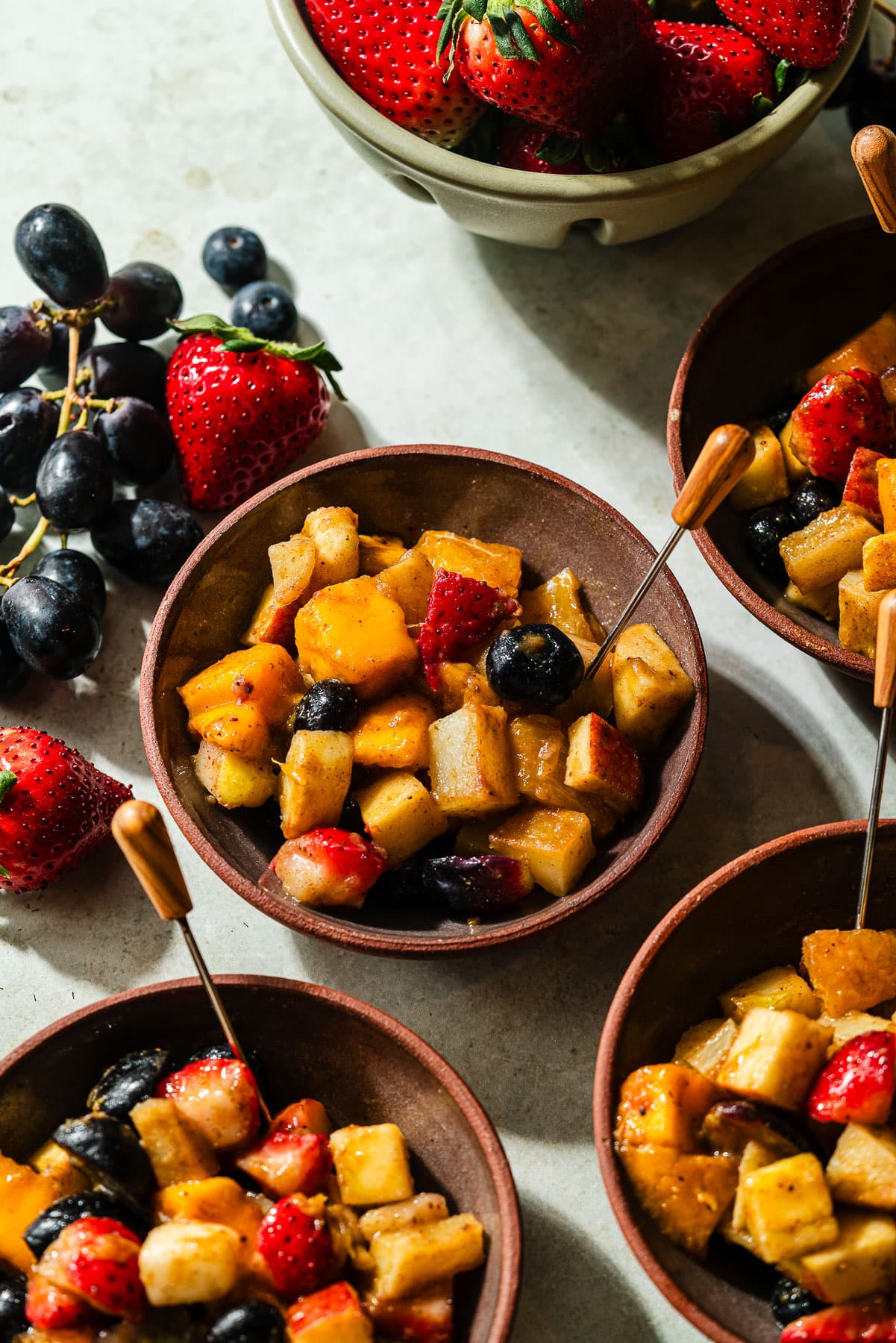 Four bowls filled with fruit chaat with an appetizer pick.