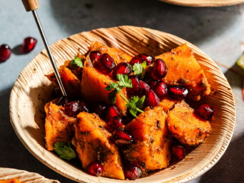 Sweet potato chaat with pomegranates in a palm leaf bowl with an appetizer pick.