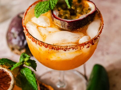 A glass of spicy passion fruit margarita garnished with fresh passion fruit and mint.