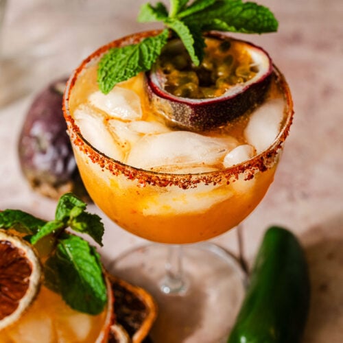 A glass of spicy passion fruit margarita garnished with fresh passion fruit and mint.