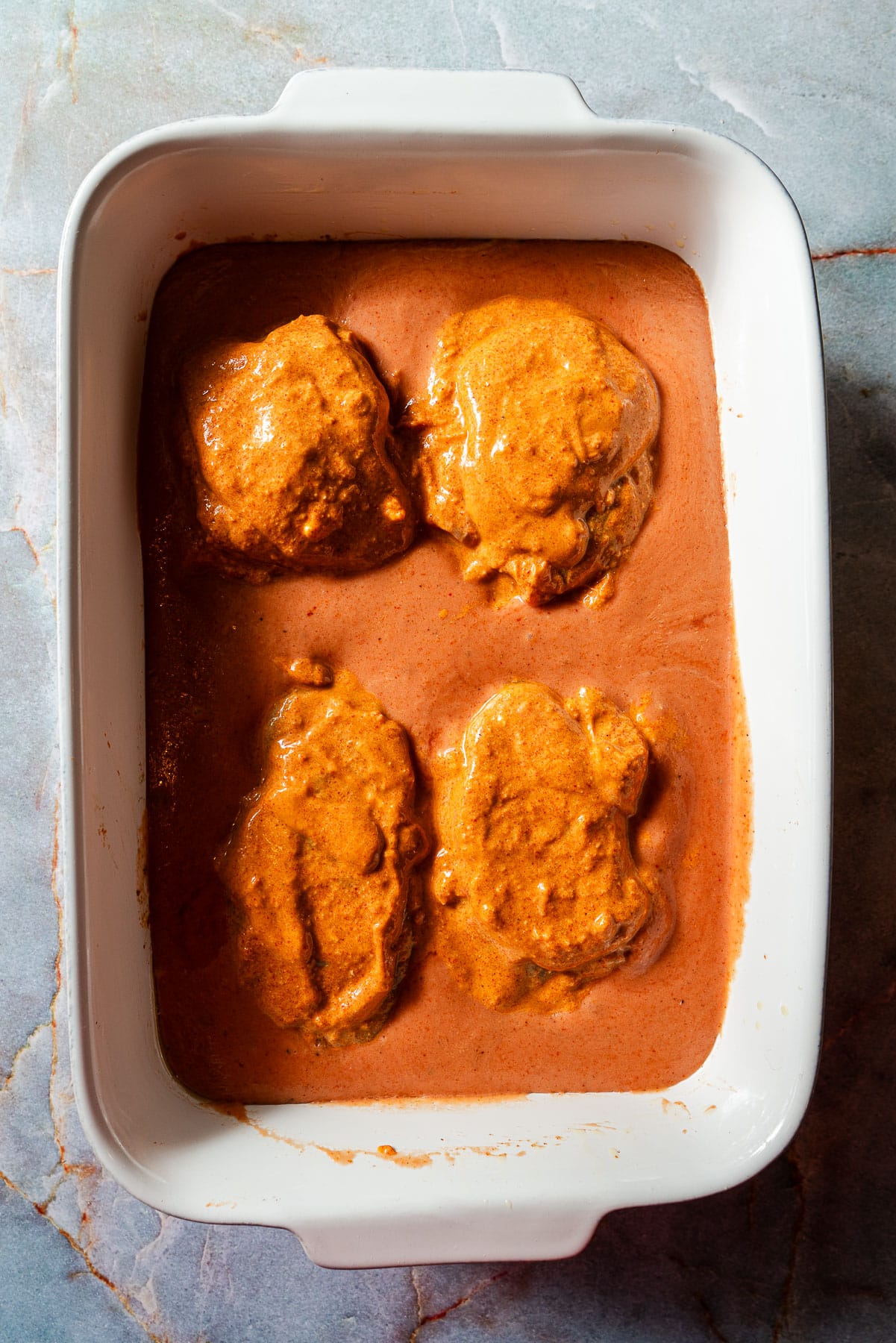 Four marinated chicken thighs in a creamy sauce unbaked in a baking dish.