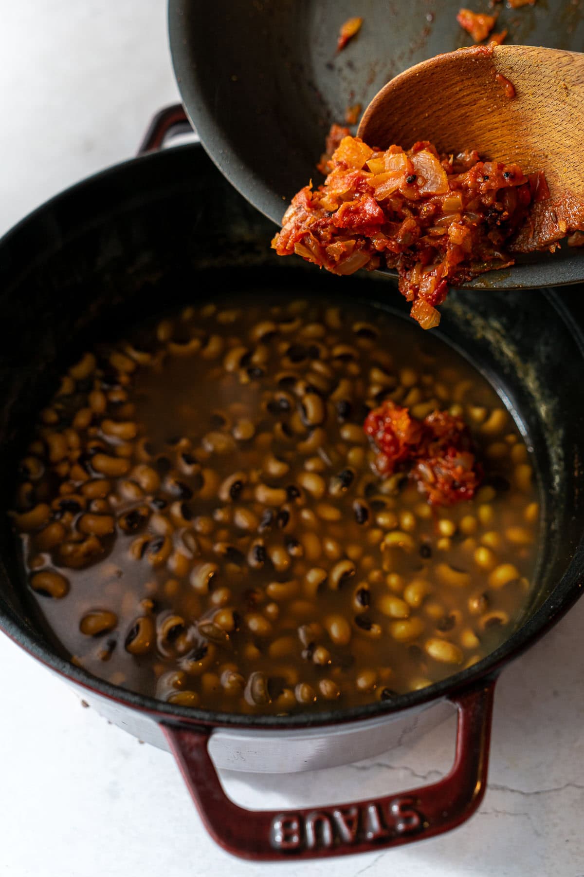 Adding cooked onion tomato masala tadka into a pot of boiled black eyed peas