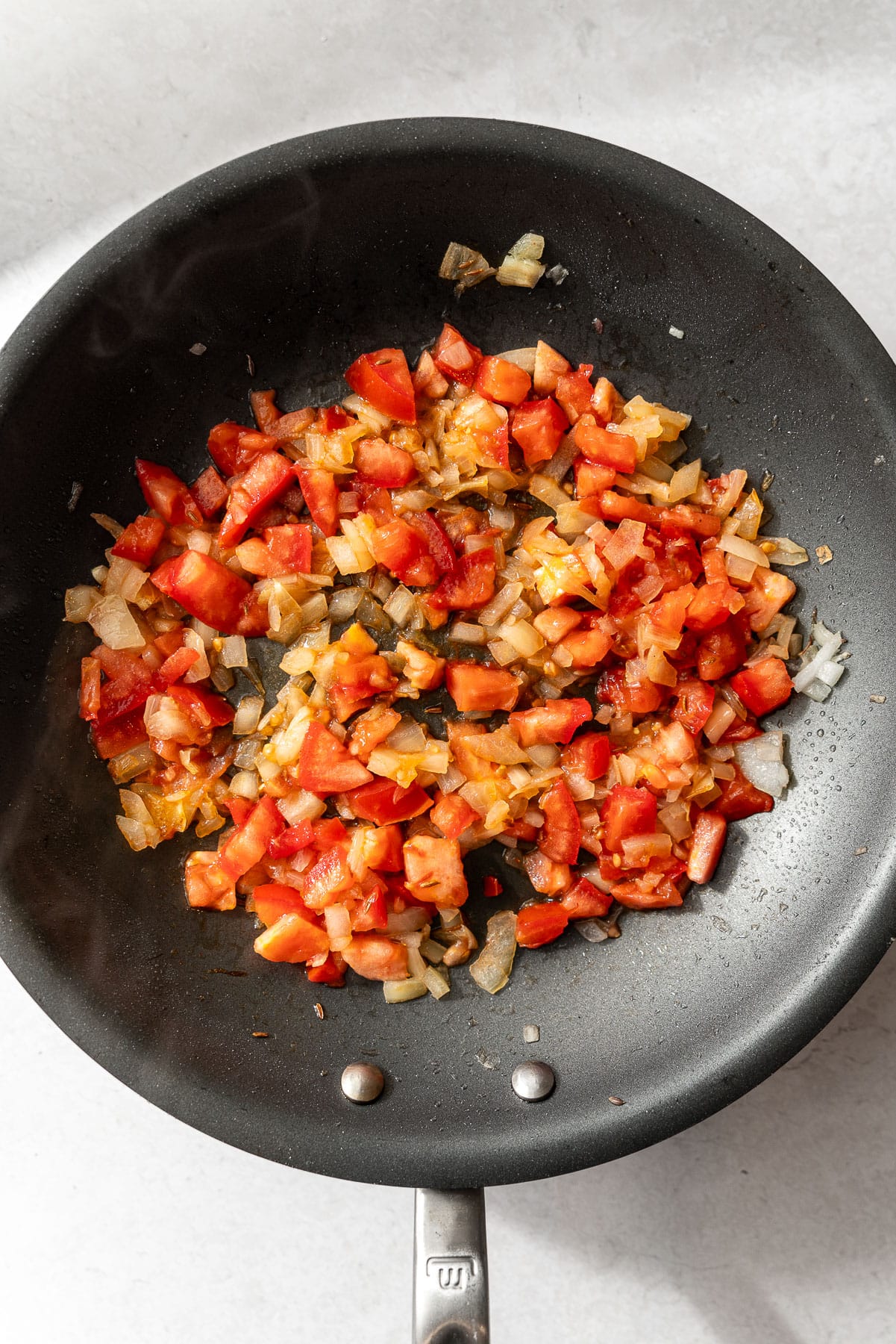 Uncooked tomato and onions in a pan.