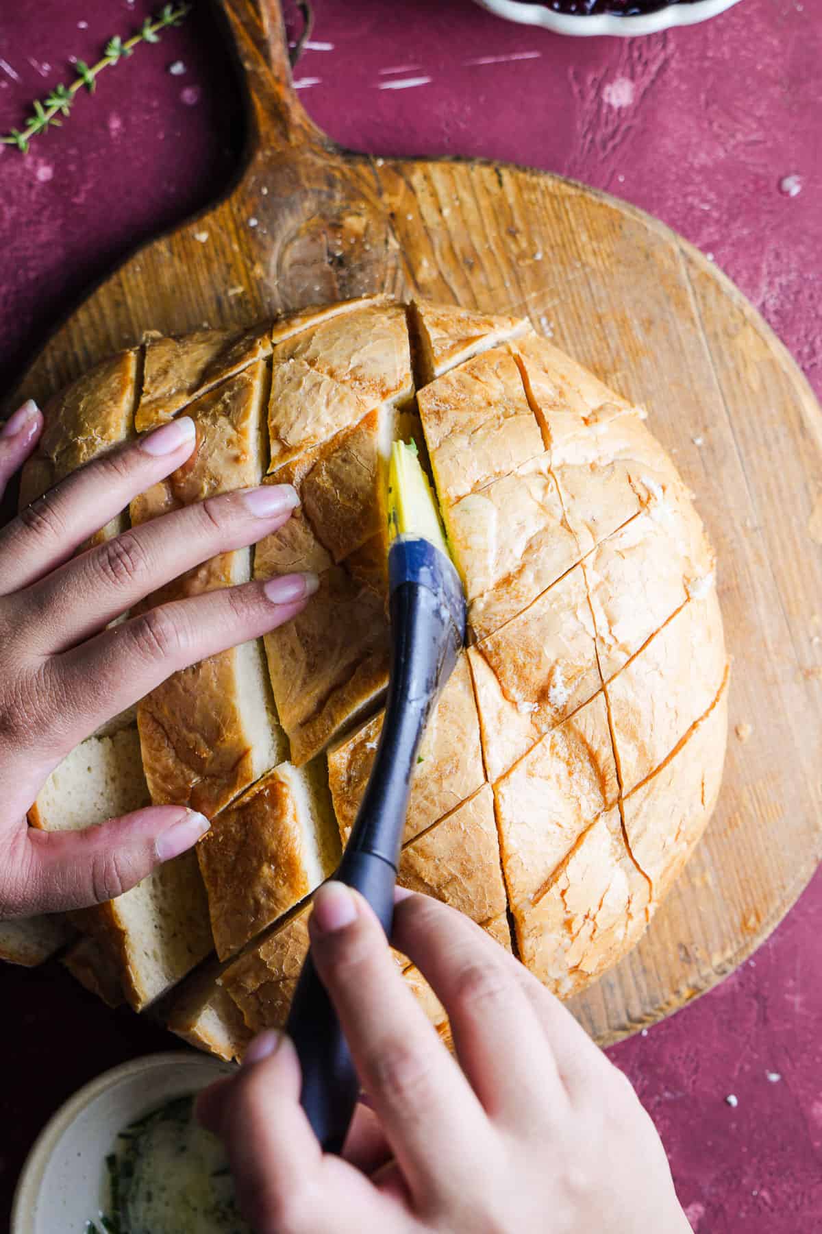 Brushing a sliced sourdough loaf with herby butter.