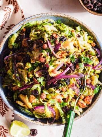 Chaat-style shaved brussels sprouts salad in a bowl with a fork and lime wedge.