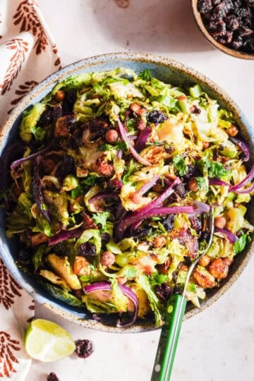 Chaat-style shaved brussels sprouts salad in a bowl with a fork and lime wedge.