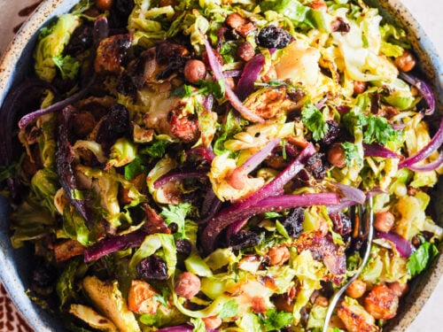 Chaat-style shaved brussels sprouts salad in a bowl with a fork and lime wedge.