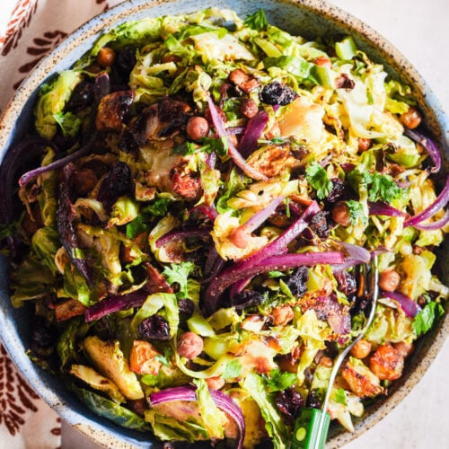 Chaat-style shaved brussels sprouts salad in a bowl with a fork and lime wedge.