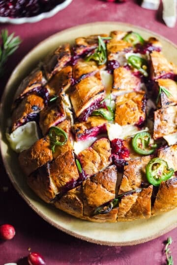 Baked loaf of bread with slices that are filled with cranberry sauce, brie, and topped with jalapeños.