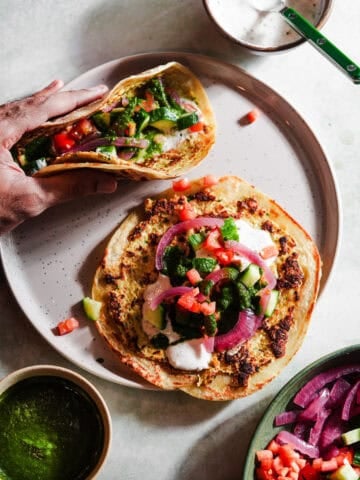 Two smashed tacos with toppings in a plate with chutney and raita.