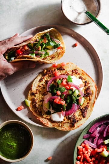 Two smashed tacos with toppings in a plate with chutney and raita.