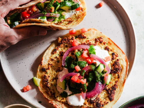 Two smashed tacos with toppings in a plate with chutney and raita.