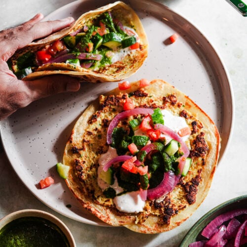 Two smashed tacos with toppings in a plate with chutney and raita.