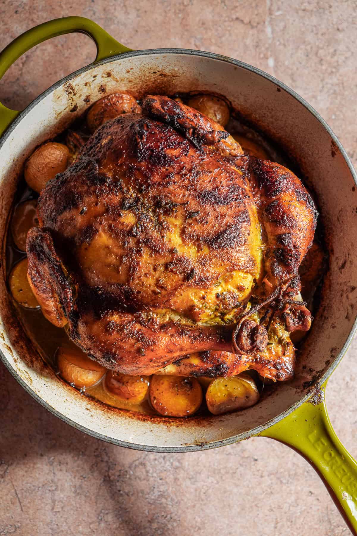 A roasted curry butter chicken on top of onions and potatoes in a dutch oven.