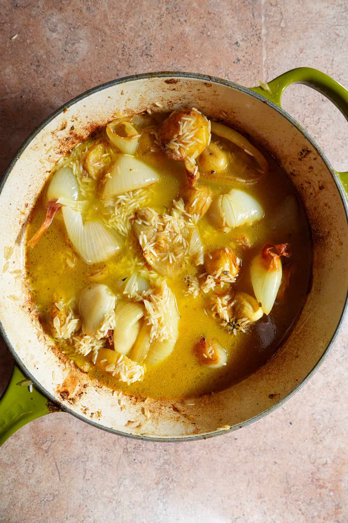 Roasted vegetables and potatoes mixed with uncooked rice in a broth.