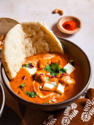Paneer Butter Masala in a Bowl with a piece of naan.