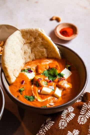 Paneer Butter Masala in a Bowl with a piece of naan.