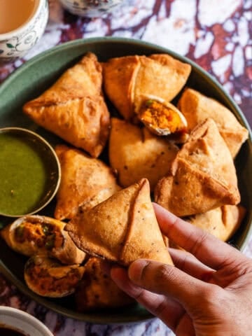A hand grabbing a samosa from a platter with chutney.