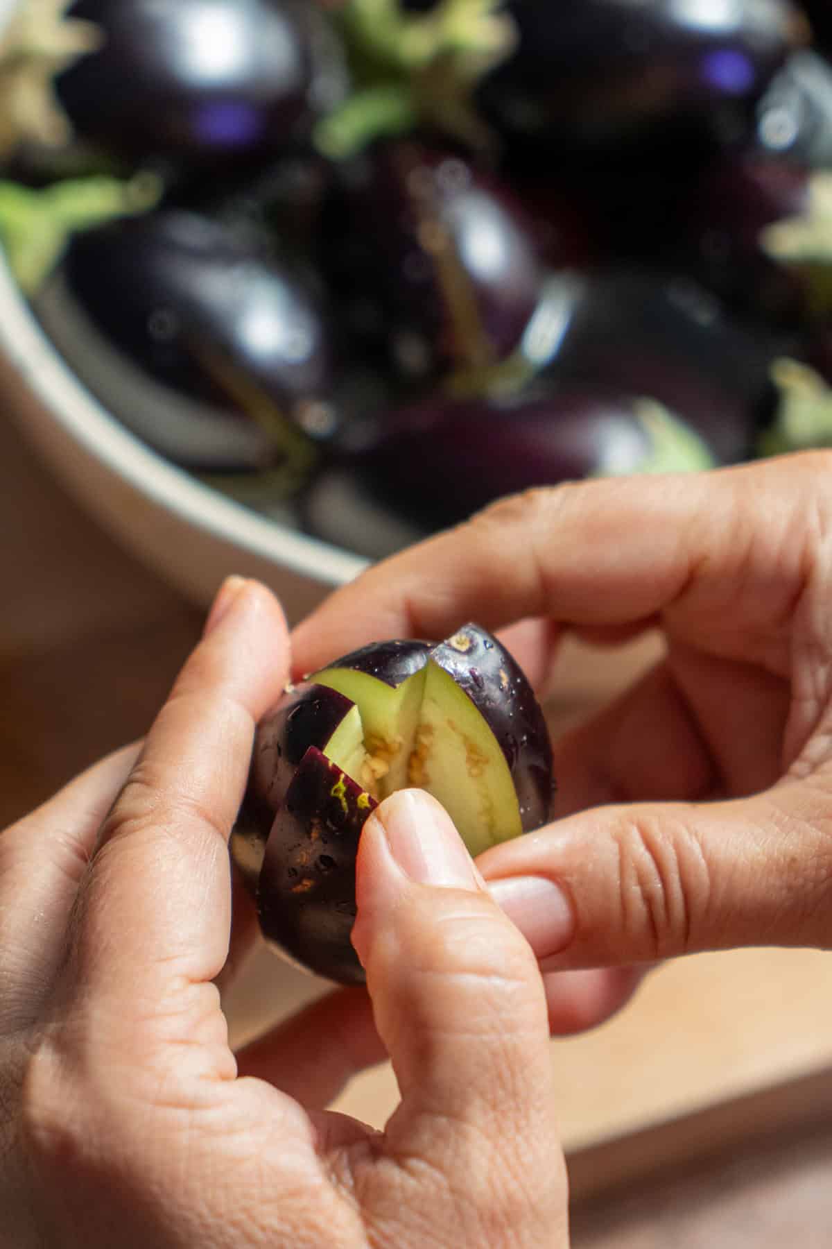 Hands holding an eggplant chopped into fours but still connected at the stem.