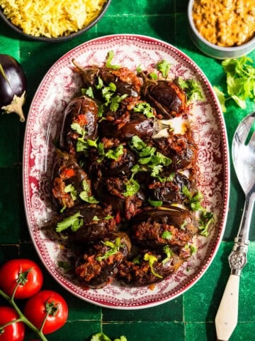 Roasted stuffed eggplant in a platter with fresh tomatoes, rice, and dal.