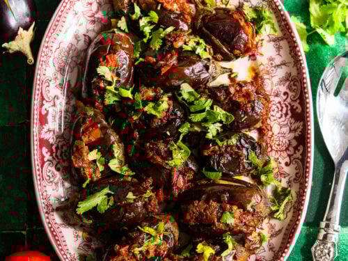 Roasted stuffed eggplant in a platter with fresh tomatoes, rice, and dal.