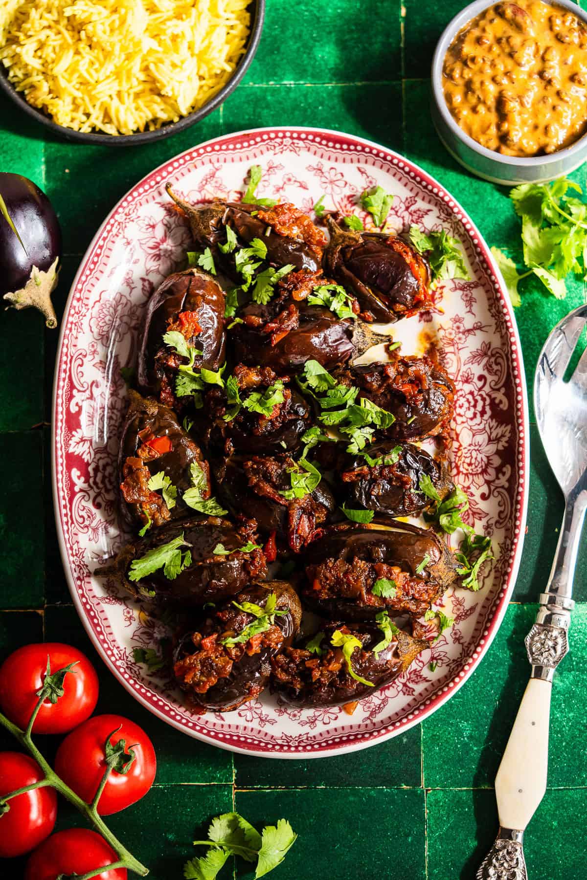 Roasted stuffed eggplant in a platter with fresh tomatoes, rice, and dal.