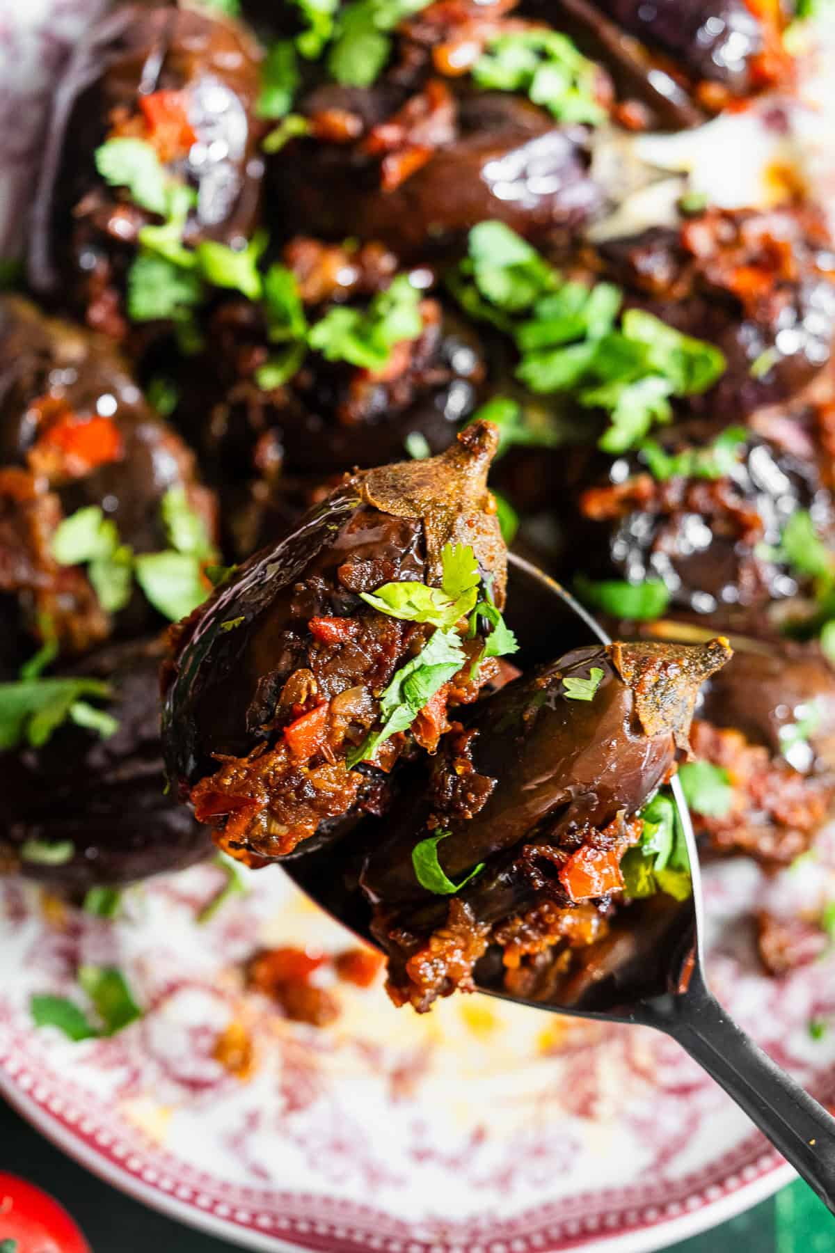 A spoon lifting up two roasted stuffed eggplant in a platter.