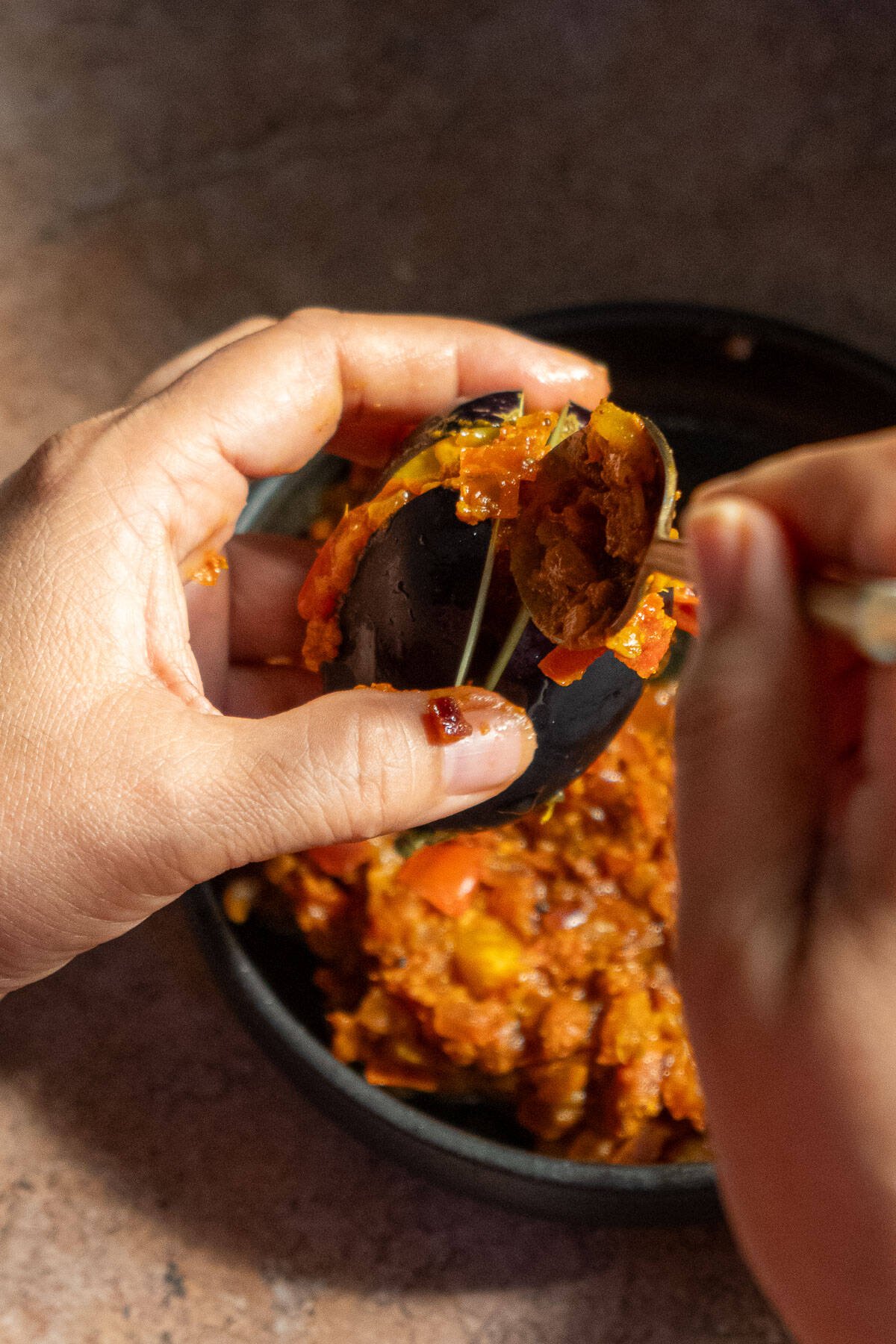 Eggplant being stuffed with onion tomato masala.