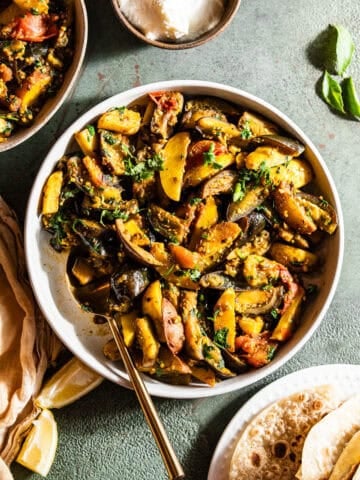 A bowl of food with potatoes, eggplant and tomatoes served with roti and dahi.