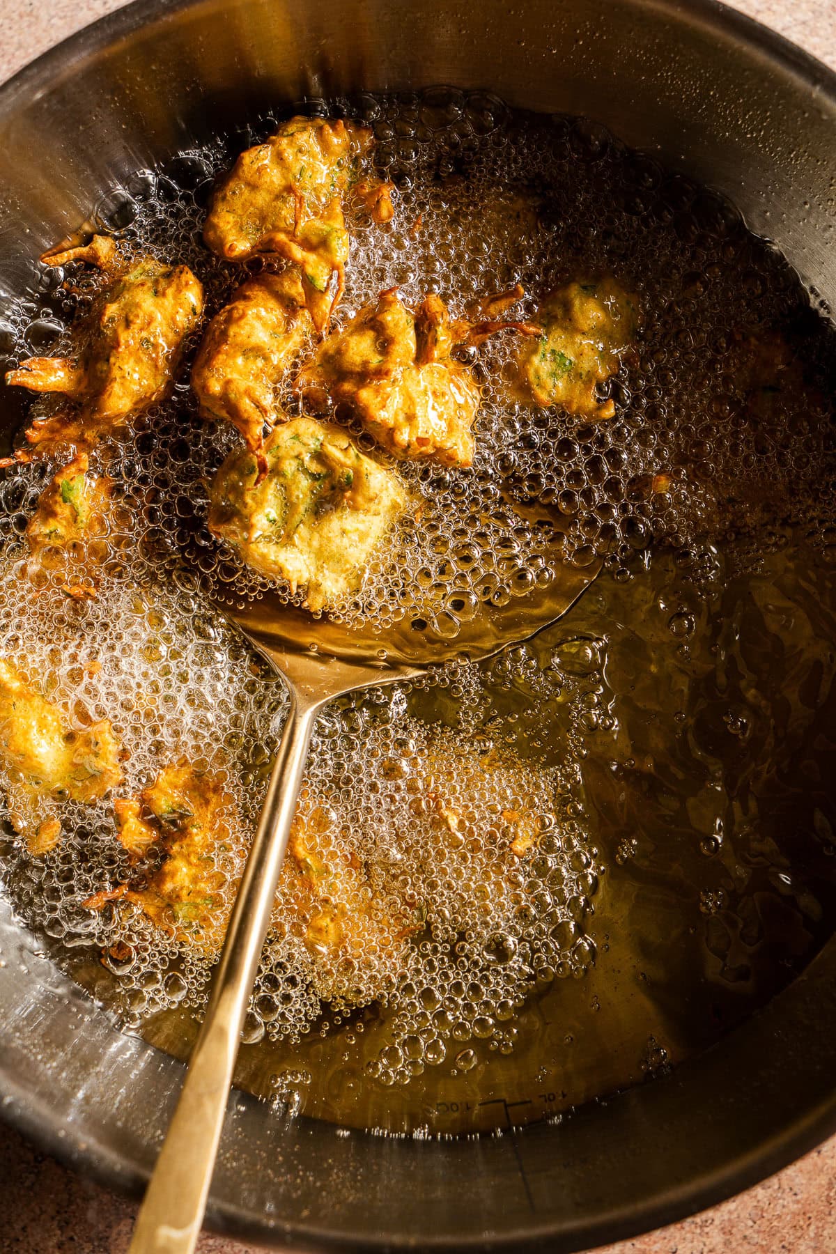 Unfried zucchini pakoras in a kadhai with oil.