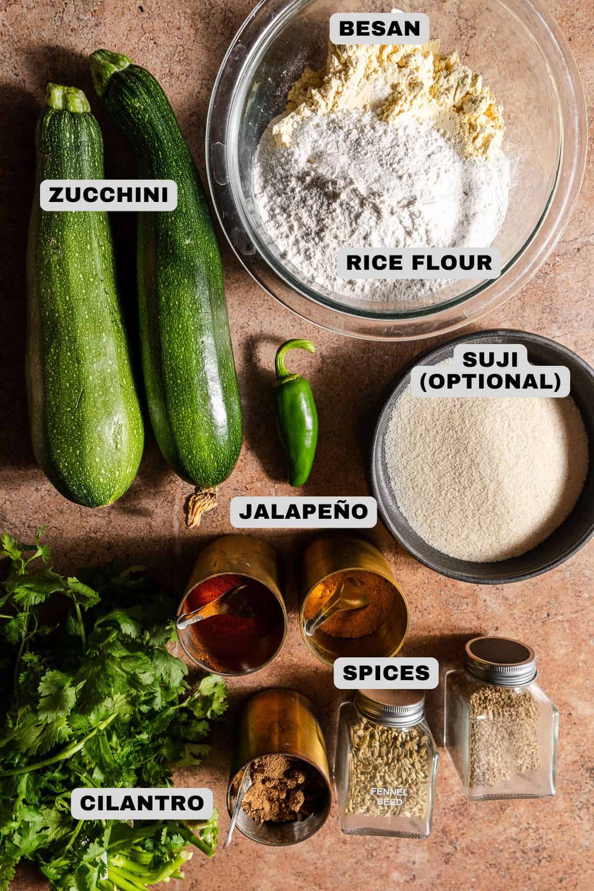 Zucchini, besan, rice flour, suji, jalapeño, spices, cilantro ingredients with labels.