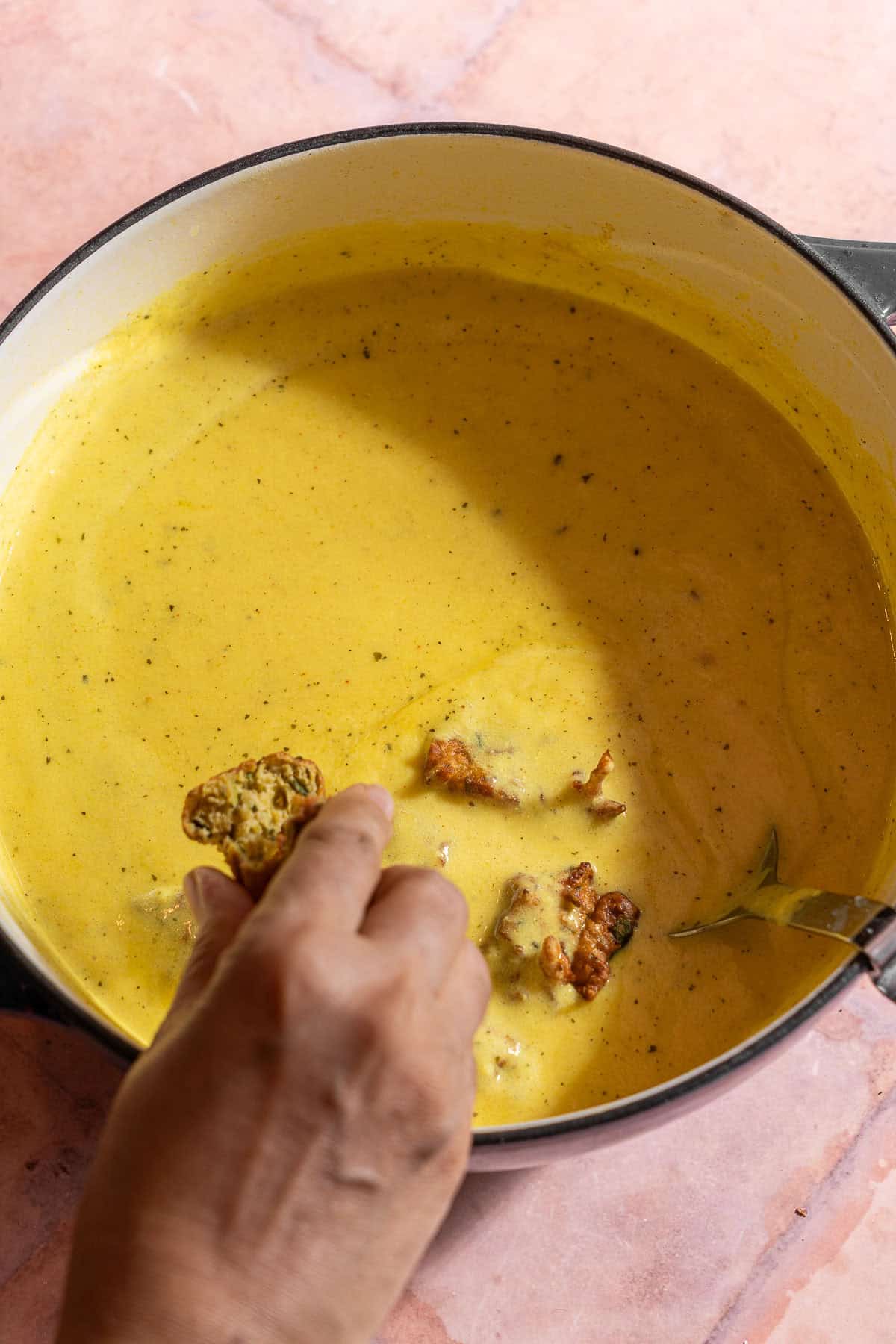 Slightly breaking apart pakora and plopping them into the base of kadhi.