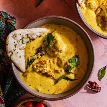 Two bowls of curry with bread and vegetables.